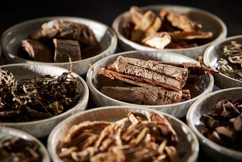Ceramic bowls holding dried Chinese herbs, bark and sliced roots used to prepare custom herbal formulas